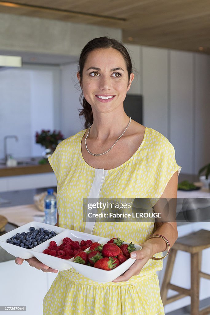 Woman holding a tray of assorted berries and smiling at home