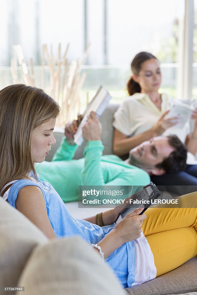 Girl using a digital tablet with her parents reading books at home