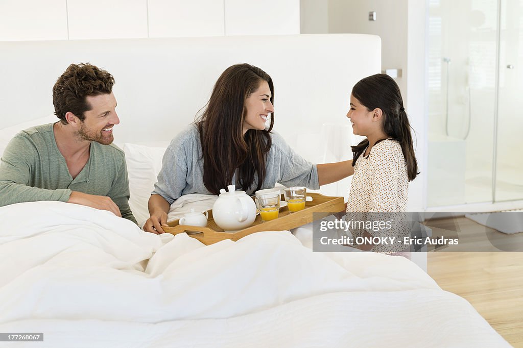 Girl serving tea to her parents on the bed