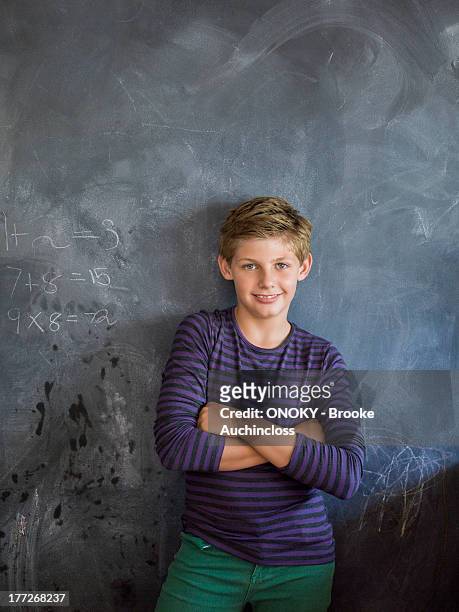 boy smiling with his arms crossed in front of a blackboard in a classroom - 12 12 12 2013 film stock-fotos und bilder