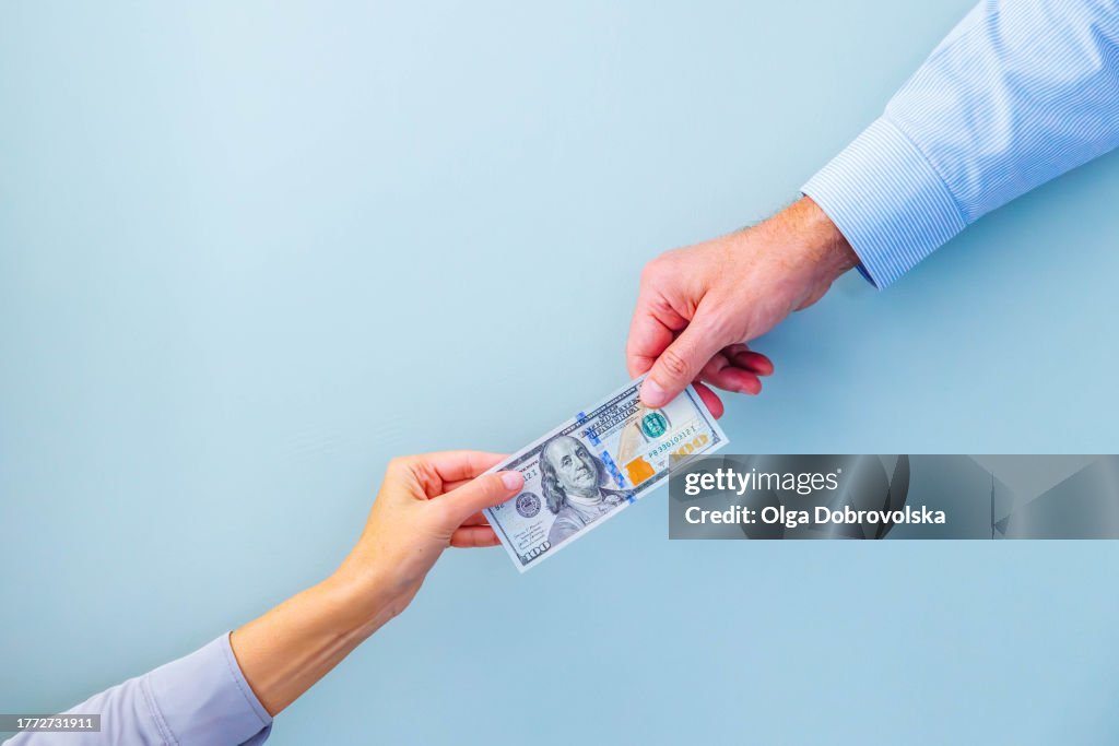 Hands of two people holding a one hundred dollars banknote on a light blue background