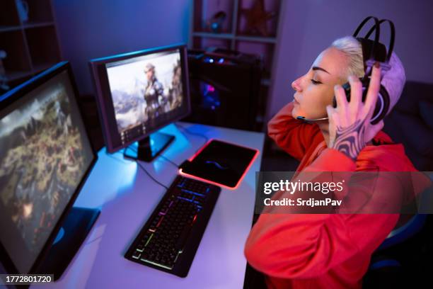 urban young caucasian female gamer, adjusting headset while playing video games on computer - heroes icon stock pictures, royalty-free photos & images