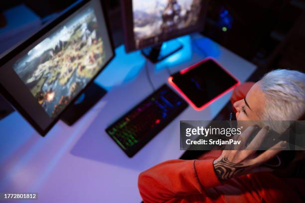 modern young caucasian female gamer, adjusting headset while playing video games on computer - heroes icon stock pictures, royalty-free photos & images