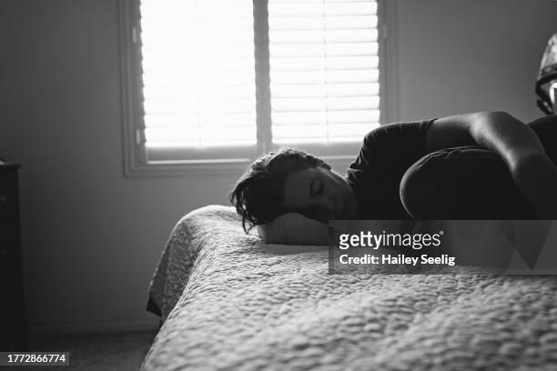 woman curled up on bed - woman curled up stock pictures, royalty-free photos & images
