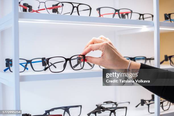 hand of unrecognizable woman reaches out to touch pair of eyeglasses lying on display - bril stockfoto's en -beelden