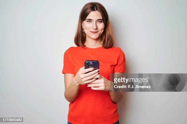 portrait of woman in red t-shirt using mobile phone on white background - shirt fotografías e imágenes de stock