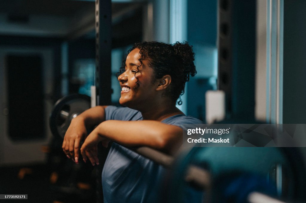 Smiling young woman leaning on barbell at health club