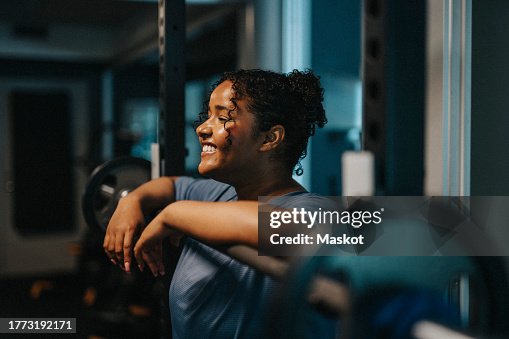 Smiling young woman leaning on barbell at health club Smiling young woman leaning on barbell at health club