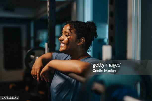 smiling young woman leaning on barbell at health club - kleine scherptediepte stockfoto's en -beelden
