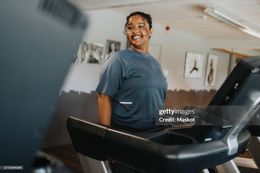 Happy young woman exercising on treadmill at health club
