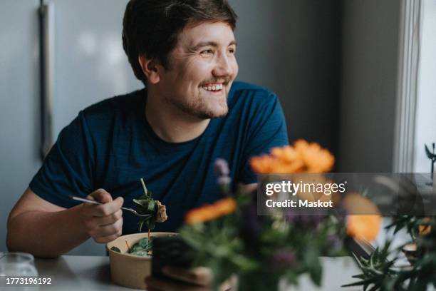 smiling young man eating meal at table - healthy food stock pictures, royalty-free photos & images