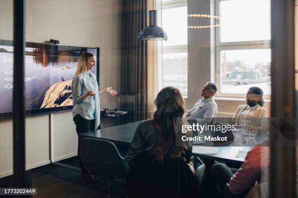 businesswoman planning strategies with male and female colleagues seen through glass of board room - palestra imagens e fotografias de stock