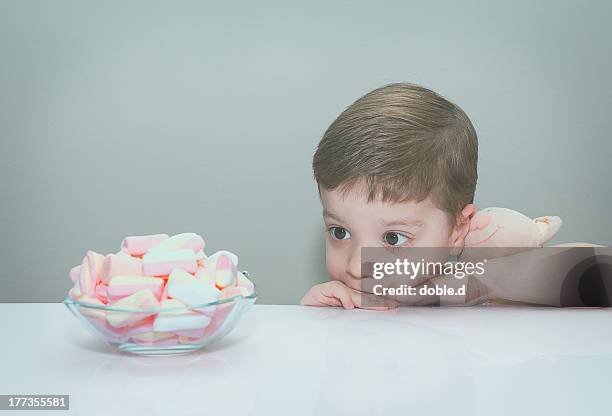 boy hugging toy, looking at bowl of marshmallows - veleiding stockfoto's en -beelden