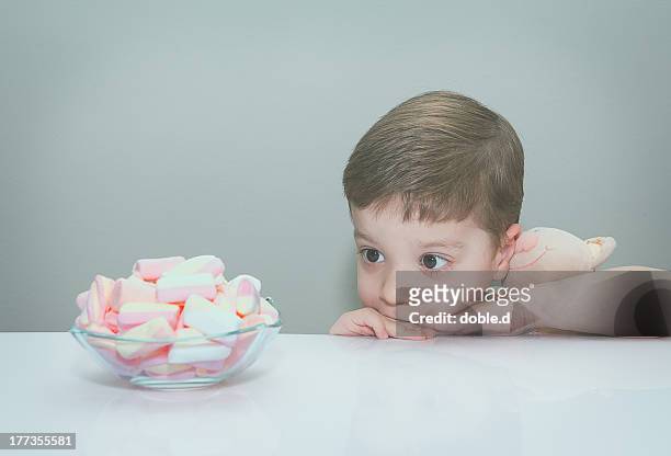 boy hugging toy, looking at bowl of marshmallows - temptation stock pictures, royalty-free photos & images