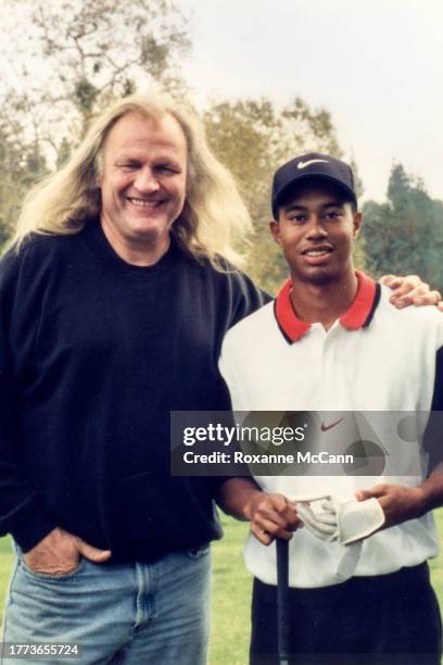 Joe Pytka and Tiger Woods who is wearing a white Nike shirt with a red collar and black sleeves, a black Nike cap and is holding golf gloves and a...