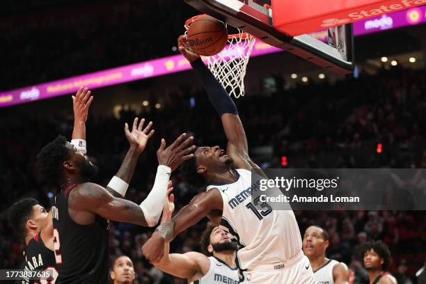 Jaren Jackson Jr. #13, right, of the Memphis Grizzlies drives to the basket past Toumani Camara, left, and Deandre Ayton, center, of the Portland...