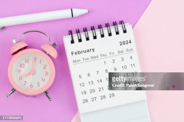 desk calendar 2024: february calendar is used to plan daily work and life with white pen and alarm clock against a two-tone background. - february stock pictures, royalty-free photos & images