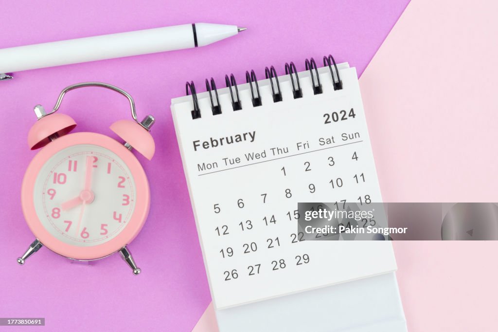 Desk Calendar 2024: February calendar is used to plan daily work and life with white pen and alarm clock against a two-tone background.