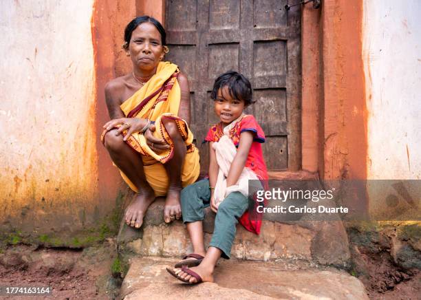 in the indian region of odisha, a grandmother from the boraparaja tribe at the door of her house with her granddaughter - geesteswetenschappen stockfoto's en -beelden