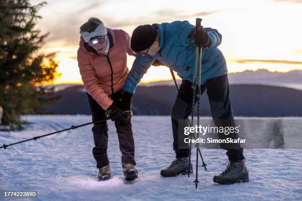 old man taking care of wife suffering with knee pain while hiking on snow - knees together 個照片及圖片檔