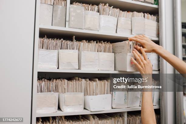 hands of woman working with patients records stored in filing cabinet - medical research paper stock pictures, royalty-free photos & images