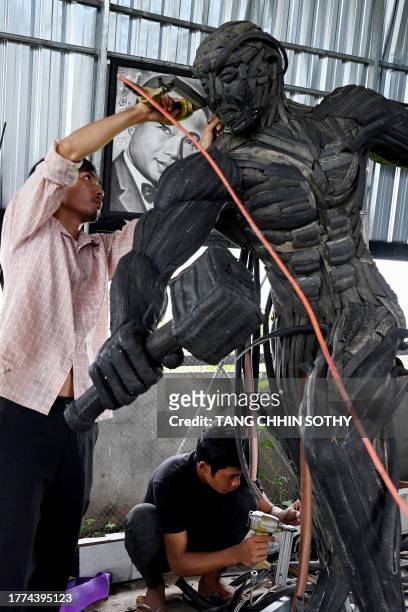 This photo taken on November 7, 2023 shows artist Mean Tithpheap and a worker making a Captain America statue using old motorbike and bicycle tyres...