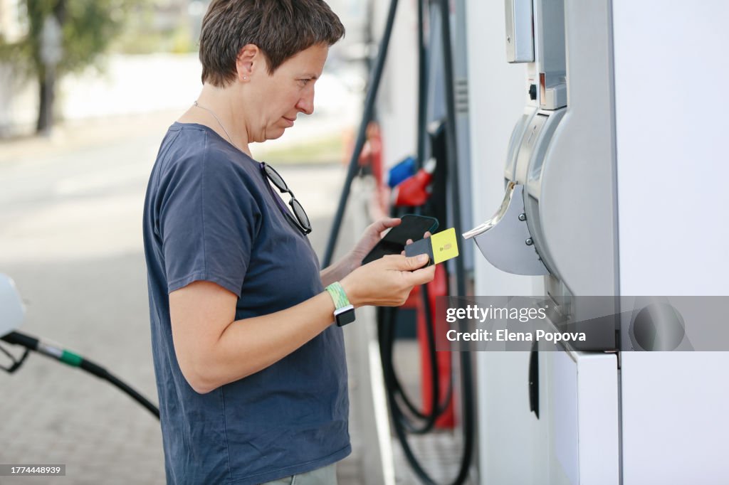 Mature Adult Woman Traveling Alone, Refueling Car At Self Service Gas Station And Paying With Credit Card