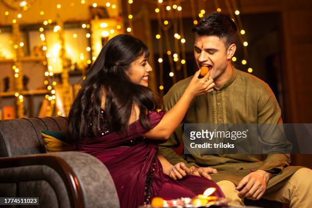 happy sister feeding sweet to her brother at home - diwali sweets stock pictures, royalty-free photos & images