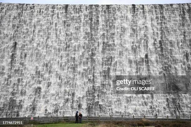 Walkers visit water flowing over Derwent Dam near Bamford in the Peak District National Park in northern England on November 10, 2023.