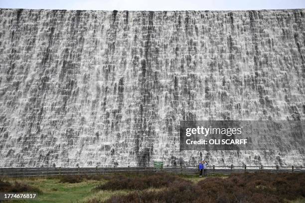 Walkers pose for a selfie photograph in front of the water flowing over Derwent Dam near Bamford in the Peak District National Park in northern...