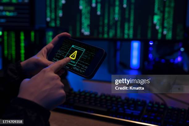 hacker hand holding mobile phone showing displaying system hacked alert. - ransomware stock-fotos und bilder