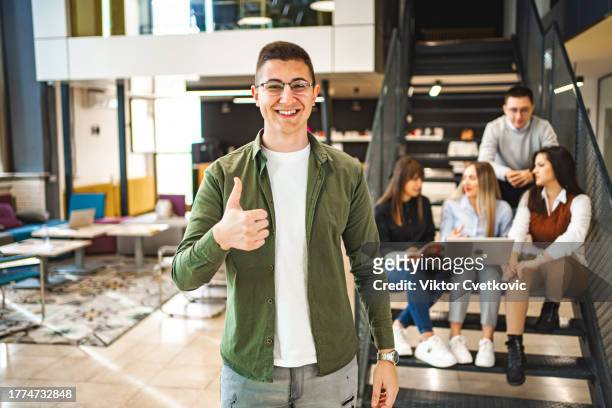 porträt eines männlichen studenten mit einer gruppe anderer studenten, die sich im hintergrund auf der treppe unterhalten - male student wearing glasses with friends stock-fotos und bilder