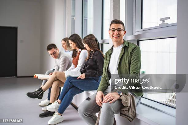 porträt eines lächelnden männlichen studenten vor einer prüfung, während andere studenten im hintergrund lernen - male student wearing glasses with friends stock-fotos und bilder