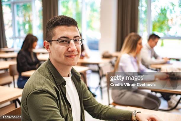 porträt eines lächelnden männlichen studenten mit brille, der in einem klassenzimmer sitzt - male student wearing glasses with friends stock-fotos und bilder