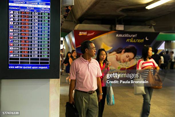 People walk by a money exchange bank kiosk on August 23, 2013 in downtown Bangkok, Thailand. The local currency dropped to its lowest level since...