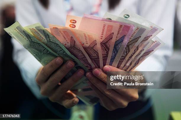 Money exchange bank teller counts Thai bhat before handing it to a customer on August 23, 2013 in Bangkok, Thailand. The local currency dropped to...