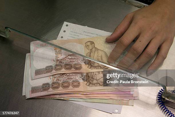 Money exchange bank teller hands over Thai bhat to a customer on August 23, 2013 in Bangkok, Thailand. The local currency dropped to its lowest level...