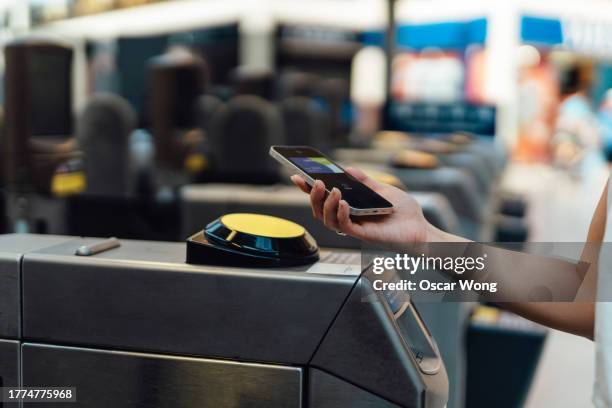 female hand making contactless payment with smartphone to pass through ticket gate at train station - london underground stockfoto's en -beelden