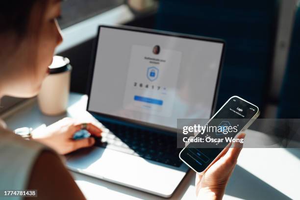 over the shoulder view of young woman logging in online account with two-factor authentication (2fa) security system visa smart phone and laptop - network security stock pictures, royalty-free photos & images