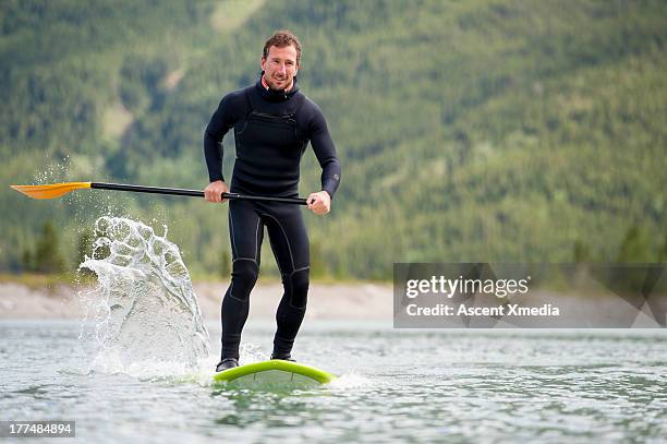 man paddleboards across mountain lake - paddle board stock pictures, royalty-free photos & images