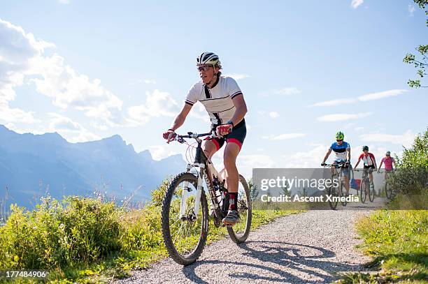 mountain bikers race along mountain pathway - ciclismo gruppo foto e immagini stock