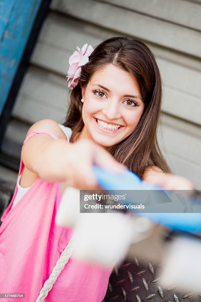 Beautiful girl holding skateboard towards camera