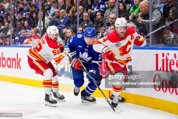 Matthew Knies of the Toronto Maple Leafs battles against MacKenzie Weegar and Rasmus Andersson of the Calgary Flames during the third period at the...