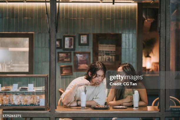 happy young asian couple dating in cafe, drinking chatting. enjoying moment together - view-through-restaurant-window stock pictures, royalty-free photos & images