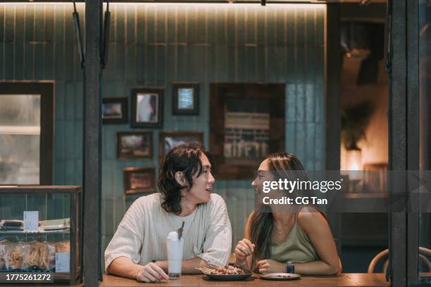 happy young asian couple dating in cafe, drinking chatting. enjoying moment together - view-through-restaurant-window stock pictures, royalty-free photos & images