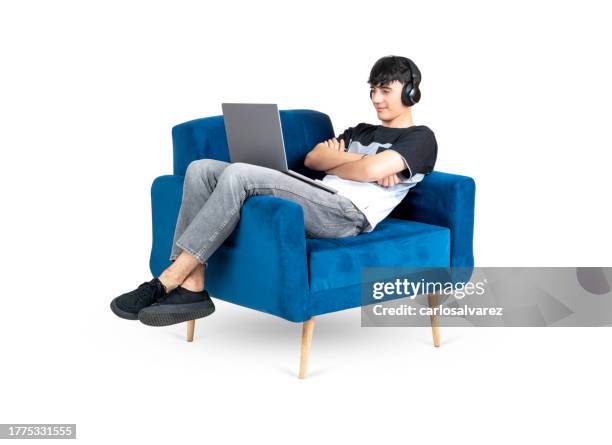 teenager using a laptop and headphone on an armchair - cross legged stock pictures, royalty-free photos & images