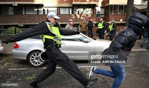 Police officer chases a man through streets close to the 'National March For Palestine' in central London on November 11 as counter-protest groups...