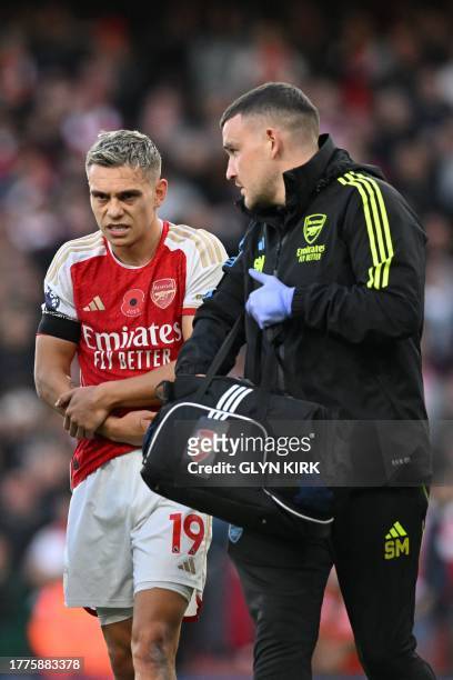 Arsenal's Belgian midfielder Leandro Trossard is helped from the pitch after hurting his arm in scoring the opening goal during the English Premier...