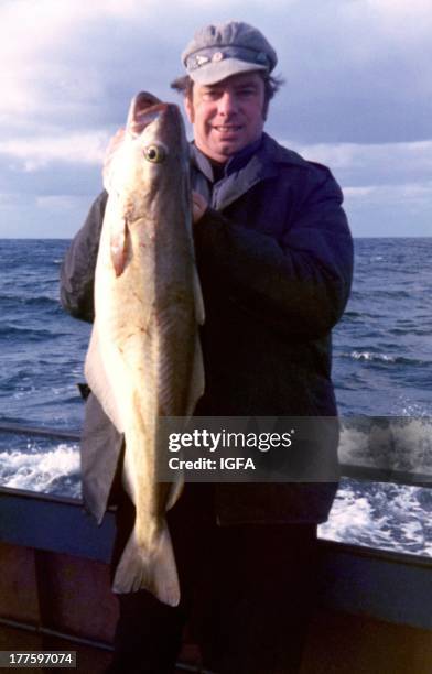 Man stands in a boat holding a 20 pound pollack caught in waters near South Devon, England on January 20, 1983.