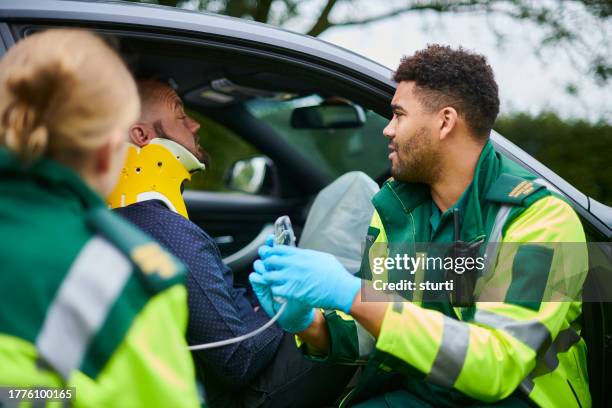 paramedics administering oxygen at car crash - pessoal de ambulância imagens e fotografias de stock